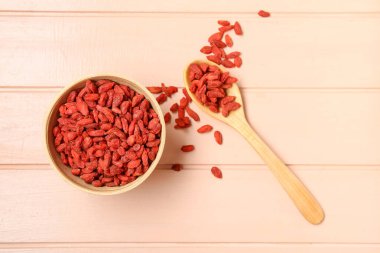 Kase ve kaşık pembe ahşap arka planda kırmızı kurutulmuş kurt üzümü.