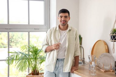 Mutfakta filtre sürahi ve bir bardak taze su olan genç bir adam.