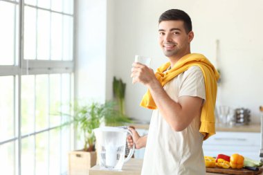 Mutfakta filtre sürahi ve bir bardak taze su olan genç bir adam.