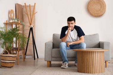 Oturma odasındaki kanepede oturan korkmuş genç adam.