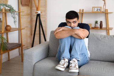 Oturma odasındaki kanepede oturan korkmuş genç adam.