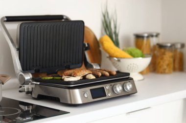 Modern elektrikli ızgarada leziz sosisler ve sebzeler mutfaktaki masada.