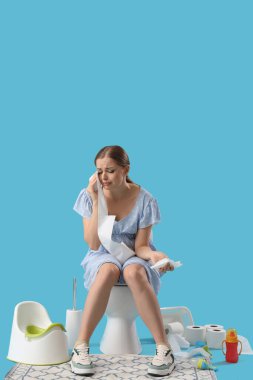 Ağlayan hamile kadın mavi arka planda klozette oturuyor.