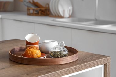 Modern mutfaktaki ahşap tepside çay seti ve tarçın rulosu, yakın plan.