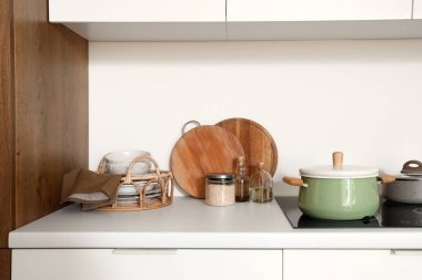 Modern mutfakta elektrikli ocak, tencere ve mutfak aletleri olan beyaz tezgah.