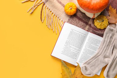 Açık kitaplı kompozisyon, sıcak çoraplar ve sarı arka planda sonbahar dekoru.