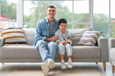 Küçük oğluyla birlikte evdeki kanepede oturan genç adam.