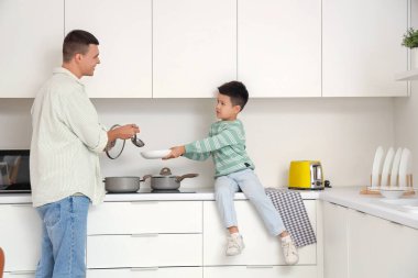 Küçük oğlu mutfakta yemek pişiren genç bir adam.