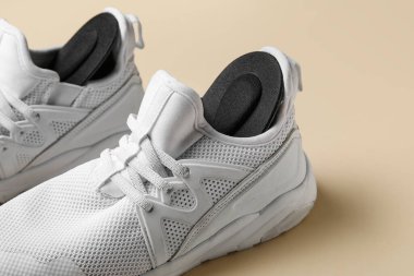 Bej arka planda siyah ortopedik tabanlı bir çift şık beyaz spor ayakkabı.