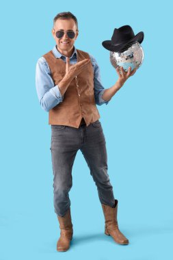 Havalı olgun kovboy mavi arka planda disko topunu işaret ediyor.