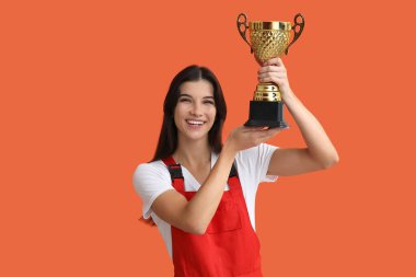 Turuncu arka planda altın bardağı olan kadın işçi.