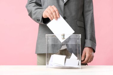 Pembe arka planda oy sandığının yanındaki genç adam, yakın plan