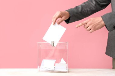 Pembe arka planda oy sandığının yanındaki genç adam, yakın plan