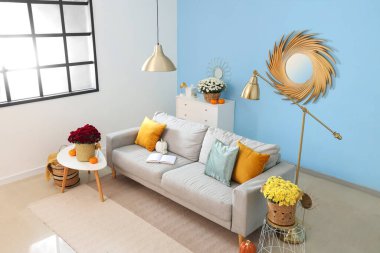 İçinde gri kanepe, balkabağı ve kahve masasında kasımpatı çiçekleri olan oturma odası.