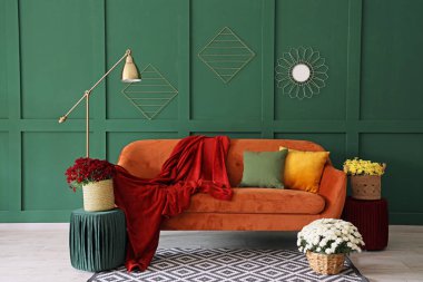 Portakal rengi kanepe ve kasımpatı çiçekleri olan modern oturma odasının içinde.