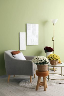 Oturma odasının içinde gri koltuk ve kahve masasında kasımpatı çiçekleri var.