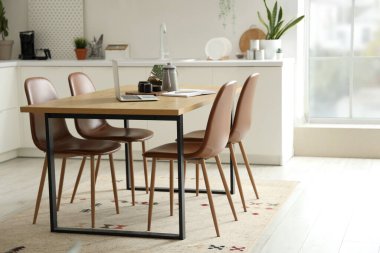 Modern mutfağın içinde dizüstü bilgisayarı, çay seti ve defter olan ahşap masa.