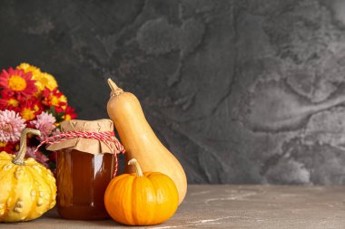 Tatlı balkabağı reçeli kavanozu ve gri masada güzel çiçekler.
