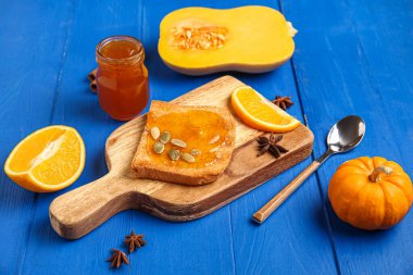 Tatlı kabak reçelli tost tahtası ve mavi ahşap arka planda tohumlar.