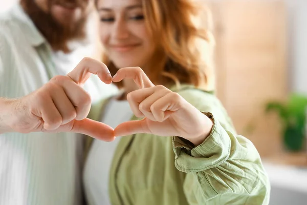 Happy couple in love making heart gesture at home, closeup