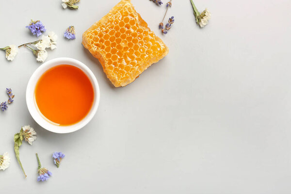Bowl with tasty honey, honeycomb and beautiful flowers on white background