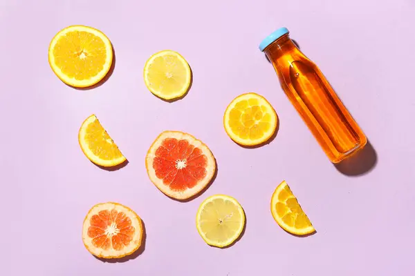 Composition with bottle of fresh lemonade and citruses on purple background