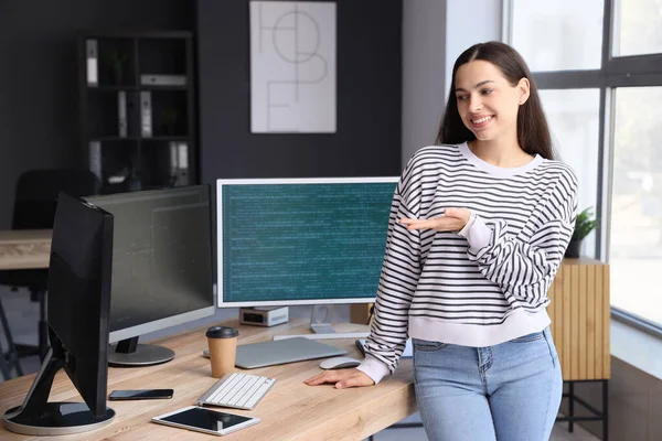 Pretty young female programmer showing something in office