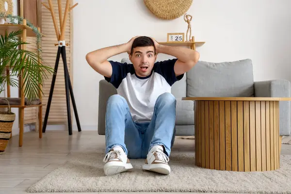 Afraid young man sitting on floor in living room at home