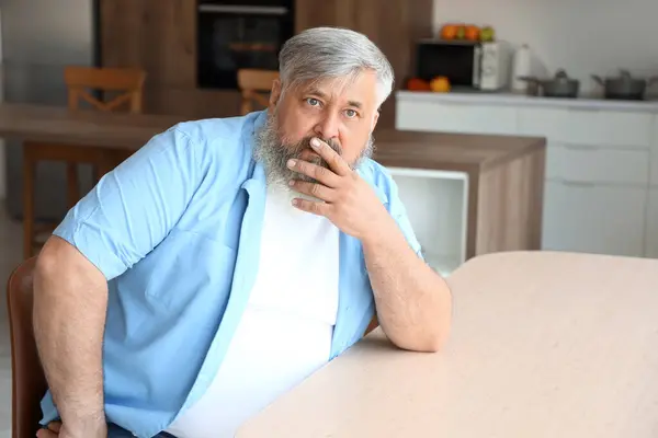 Afraid mature man at table in kitchen