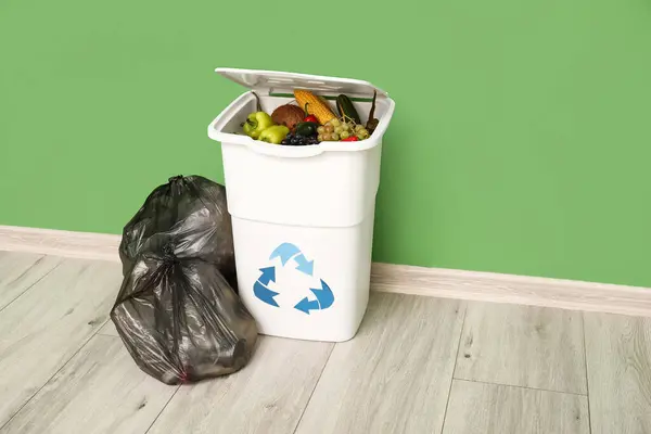 Container for trash with food waste and full garbage bags near green wall. Recycling concept