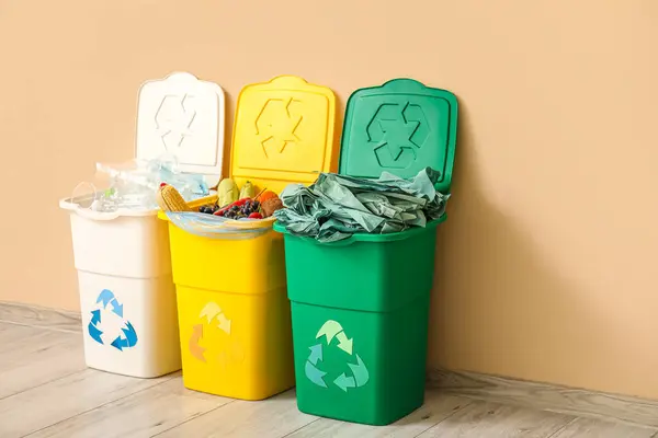 Containers for garbage with different trash near beige wall. Recycling concept