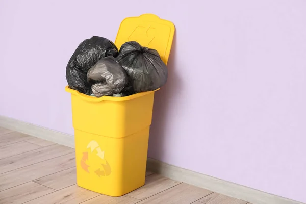 Container for trash with full garbage bags near lilac wall. Recycling concept