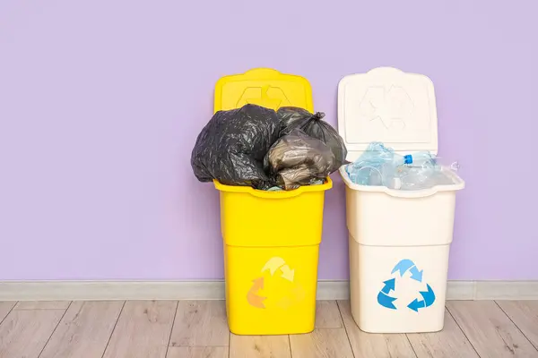 Containers for trash with full garbage bags and plastic near lilac wall. Recycling concept