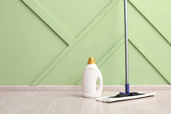 Wooden laminate floor with mop and bottle of detergent near green wall