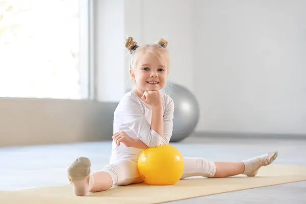 Cute little girl with gymnastic ball sitting on mat in gym