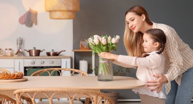 Annesi ve mutfakta laleleri olan tatlı küçük bir kız.