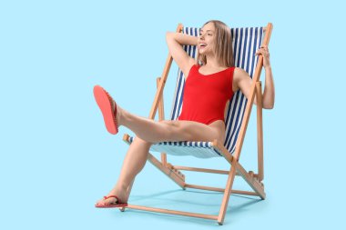 Güzel genç bayan mavi arka planda güverte sandalyesinde dinleniyor.