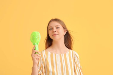 Sarı arka planda mini vantilatörü olan güzel genç bir kadın.