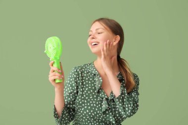 Yeşil arka planda mini vantilatörü olan güzel genç bir kadın.