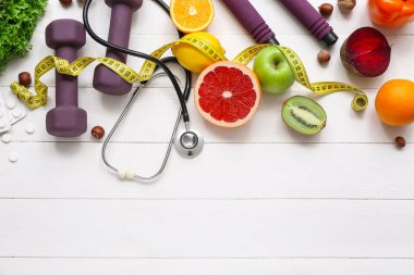 Sağlıklı ürünler, haplar, dambıllar ve beyaz ahşap arka planda steteskop.