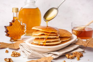 Beyaz arka planda lezzetli kreplerin üzerine akçaağaç pekmezi dökülüyor.