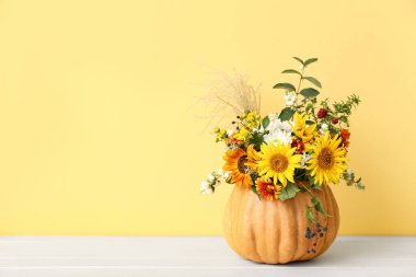Beyaz ahşap masada sarı arka planda balkabağında güzel bir sonbahar buketi.