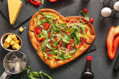 Lezzetli kalp şekilli pizza tahtası ve siyah arka planda malzemeler.
