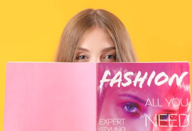 Sarı arka planda dergisi olan güzel genç bir kadın.