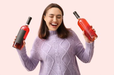 Pembe arka planda kırmızı şarap şişeleri olan güzel genç bir kadın.