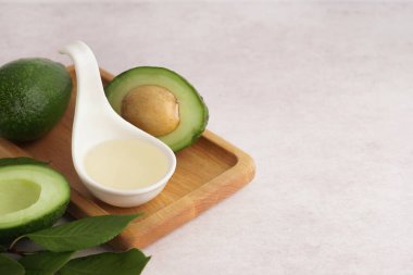 Tahta tepside taze avokadolar ve beyaz arka planda bir kaşık gerekli yağ.