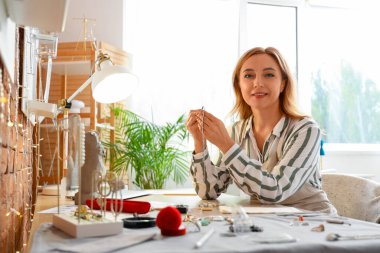 Kadın kuyumcu atölyedeki masada küpeyi inceliyor.