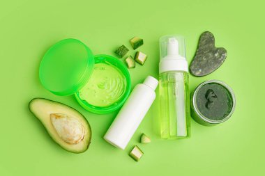 Kozmetik ürünleri, guasha masaj aracı ve yeşil arka planda avokado bileşimi