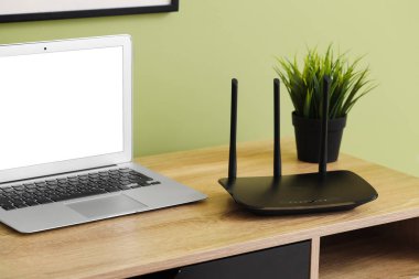 Ofisteki yeşil duvarın yanında dizüstü bilgisayarı olan modern Wi-Fi yönlendirici.