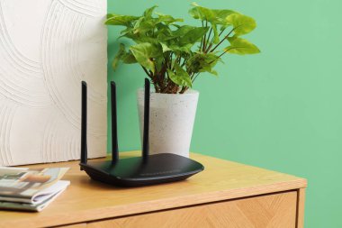 Yeşil duvarın yanındaki rafta bitki ve boya ile modern wi-fi yönlendirici